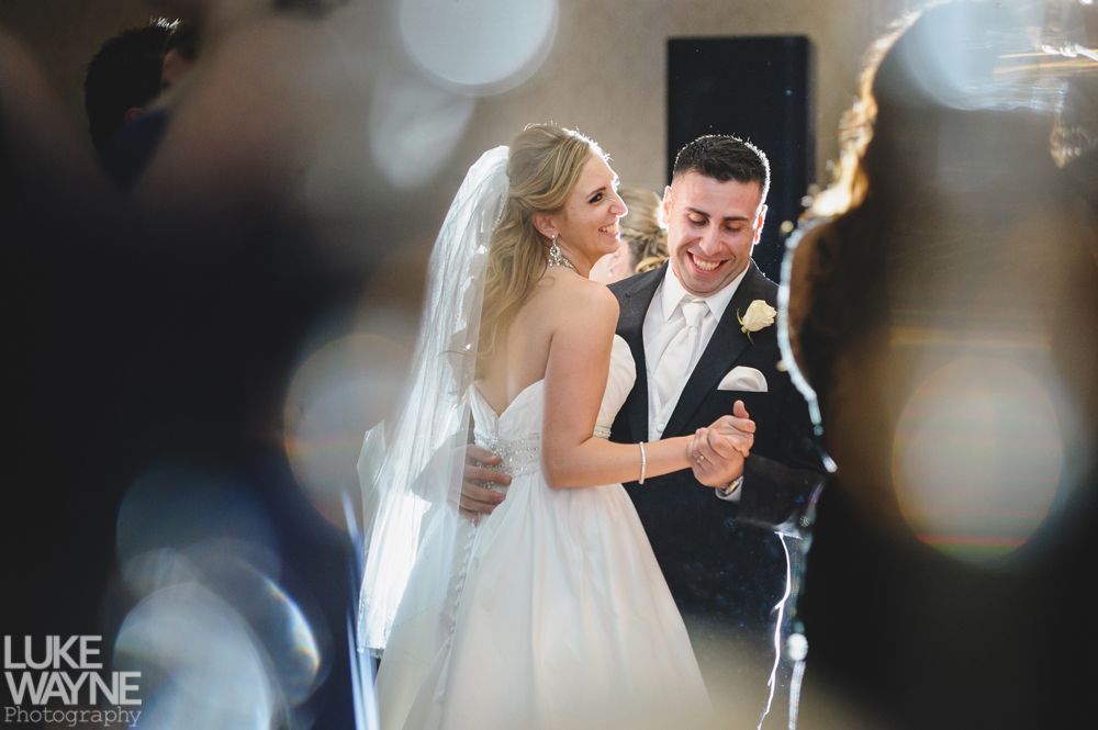 Couple in wedding attire posing in a bar. The woman's dress is white, the man's suit grey, both smiling.