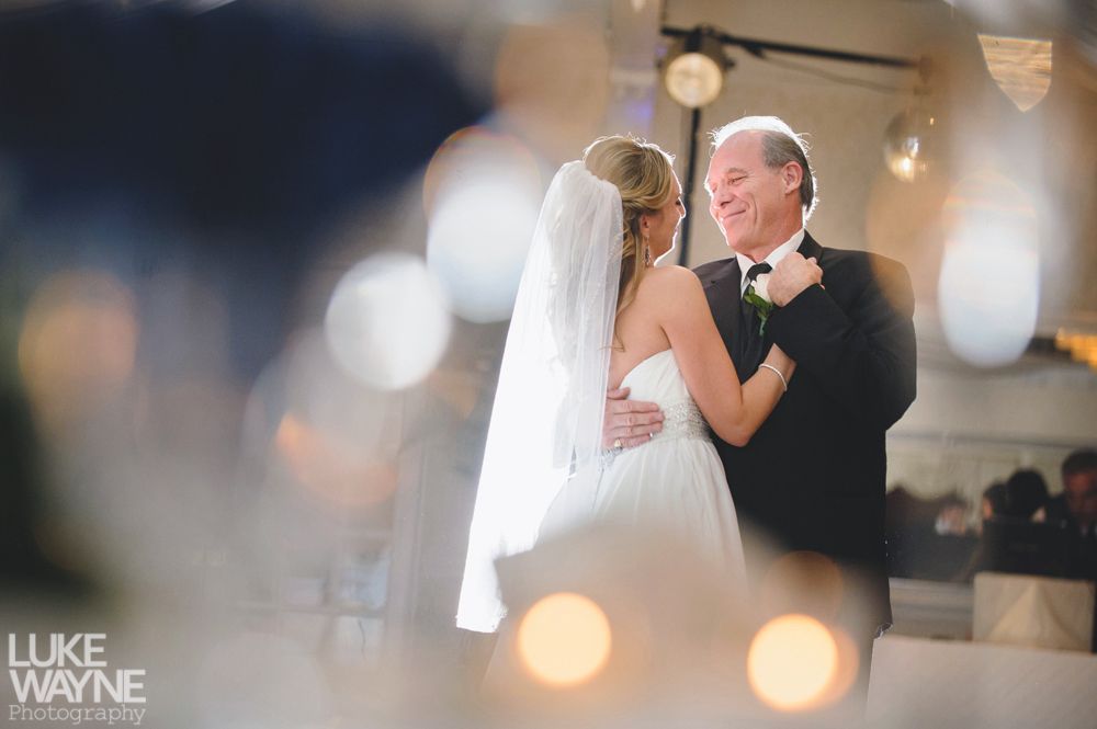 Bride and groom in wedding attire kissing in a dimly lit bar, next to a pool table.