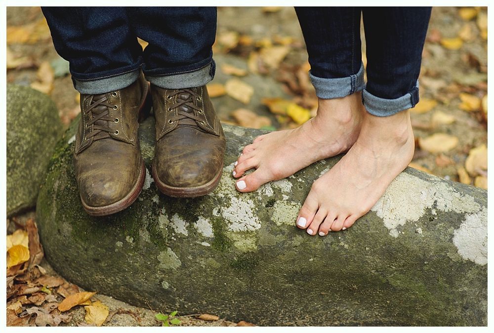 Bare feet beside work boots on a mossy rock with fall foliage.