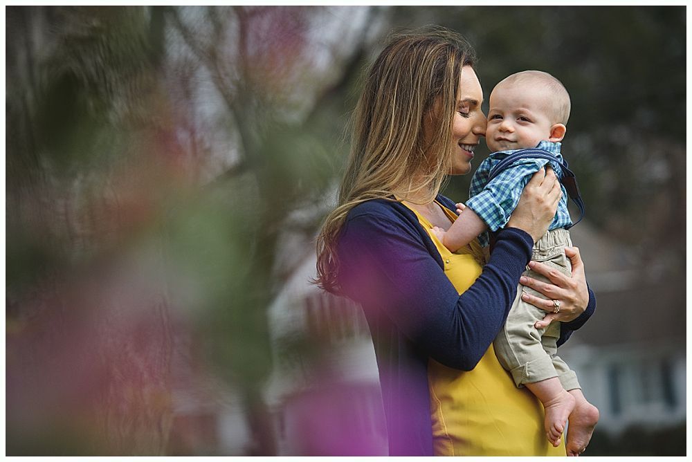 Woman in yellow dress and blue sweater holds a smiling baby outside.