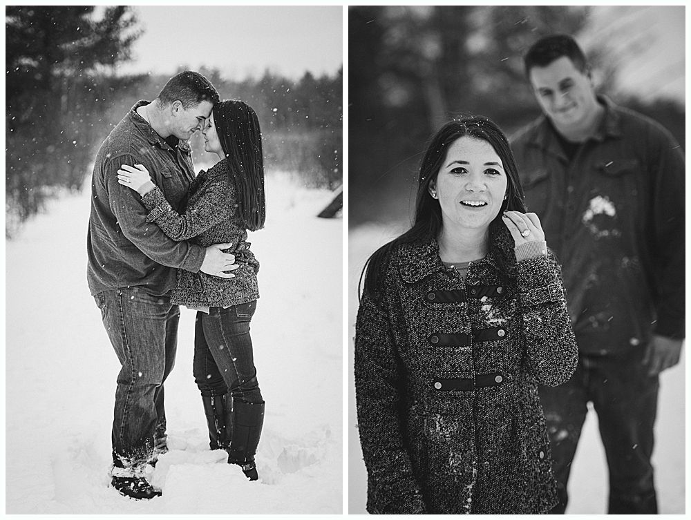 Couple embraces in snowy field; woman smiles, man in background. Black and white.