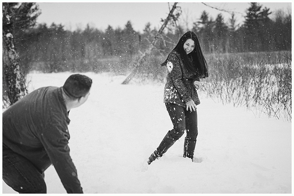 Person throwing snowball at another person in a snowy field with trees in the background.