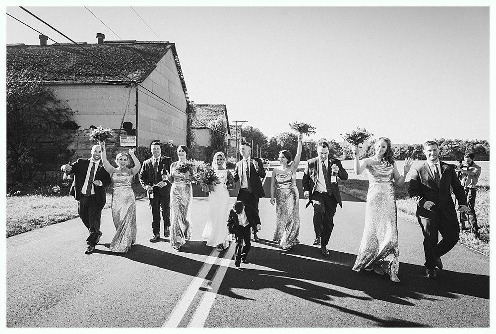 Wedding party walking down a road with bouquets raised. Black and white photo.