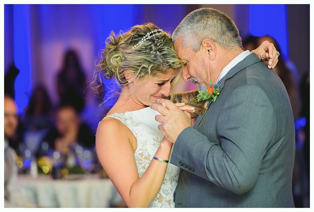 Bride and father share an emotional dance at wedding reception, both with heads touching and eyes closed.
