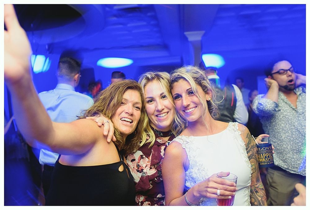 Three smiling people taking a selfie at a party under blue lights.