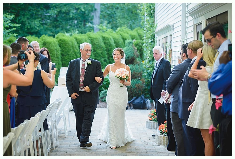 Bride with arms up, making a funny face, groom looking at his hand, cake cutting in background.