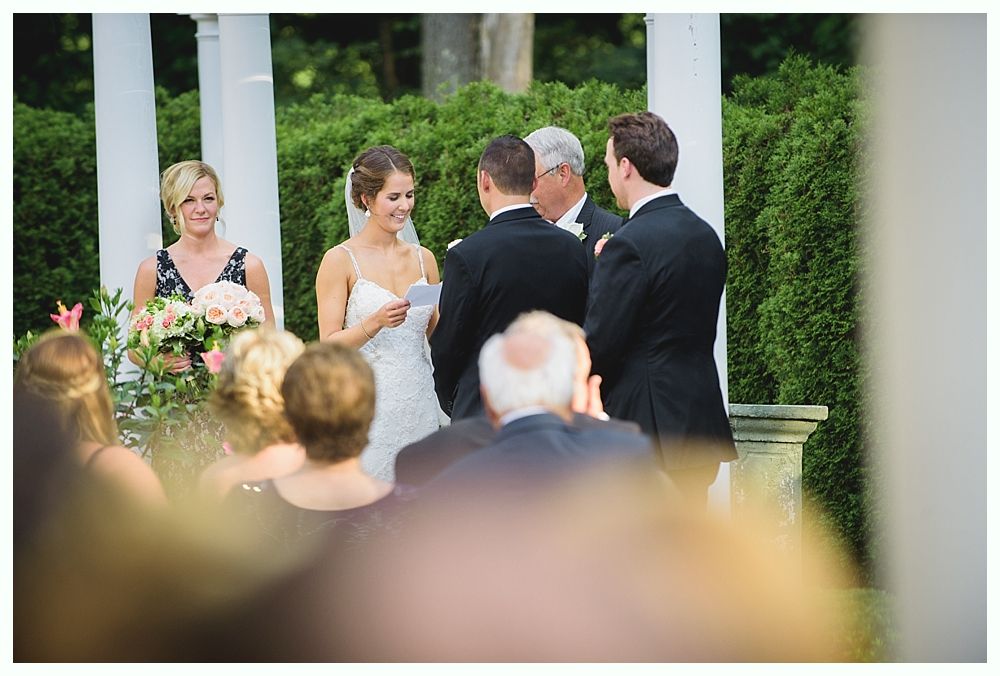 Bride with arms up, making a funny face, groom looking at his hand, cake cutting in background.