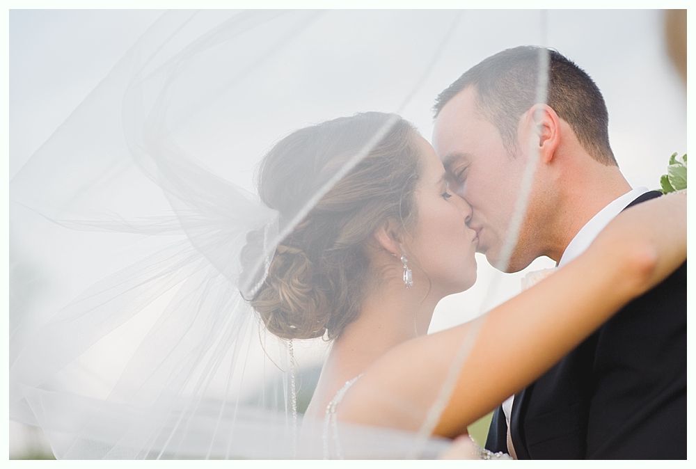 Bride with arms up, making a funny face, groom looking at his hand, cake cutting in background.