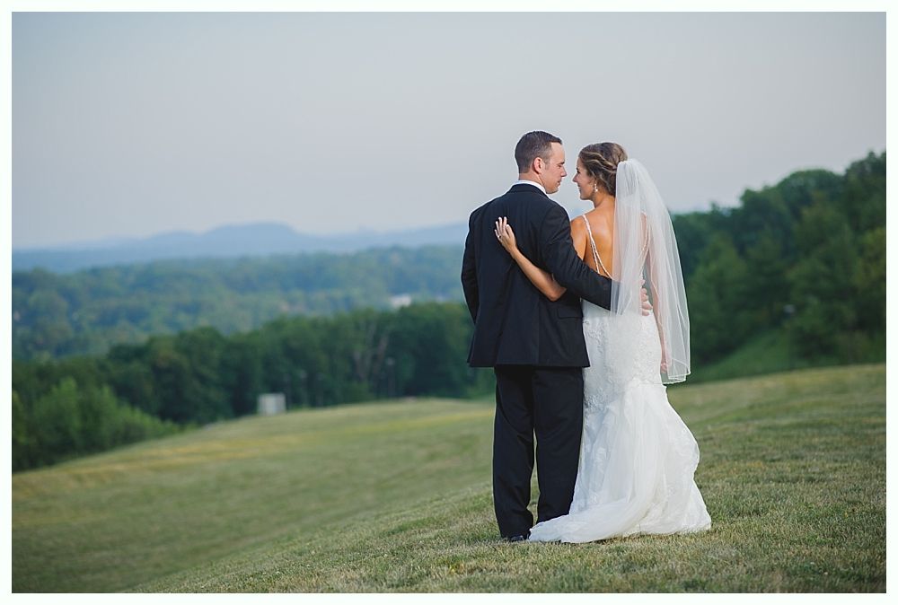 Bride with arms up, making a funny face, groom looking at his hand, cake cutting in background.