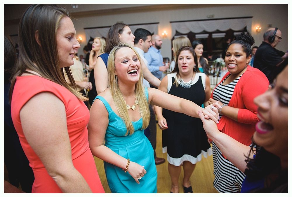 Bride with arms up, making a funny face, groom looking at his hand, cake cutting in background.