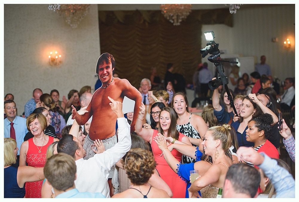Bride with arms up, making a funny face, groom looking at his hand, cake cutting in background.