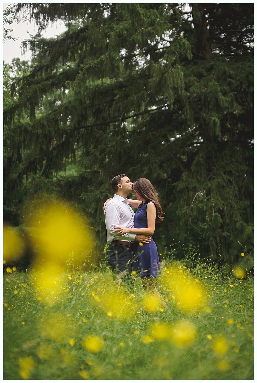 Groom laughs, bride and woman in pink stand on a bridge decorated with flowers.