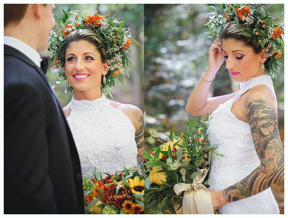 Bride with flower crown and arm tattoos, smiling at groom, holding bouquet. Outdoor wedding.