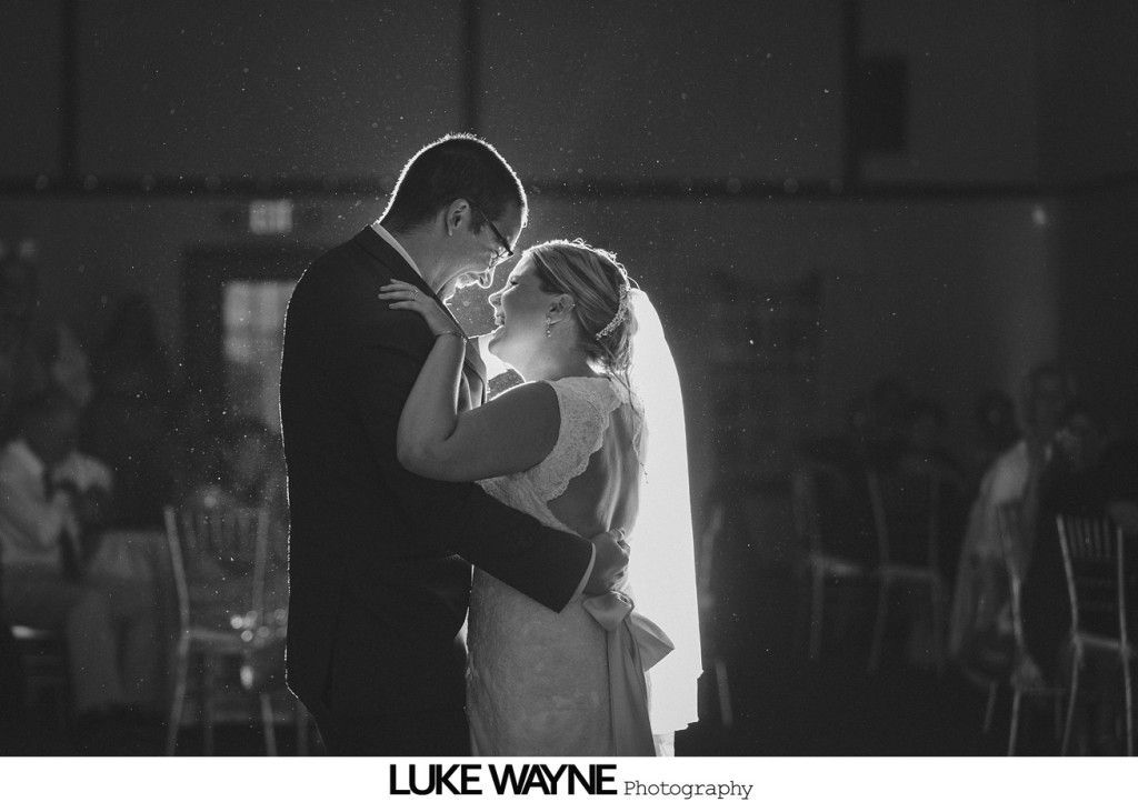 Bride and groom dance closely, illuminated by a back light, during a wedding reception.