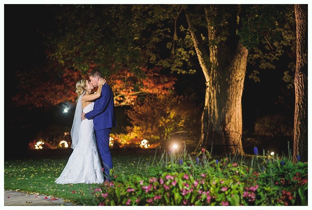 Bride and groom kissing outdoors at night, under a tree.
