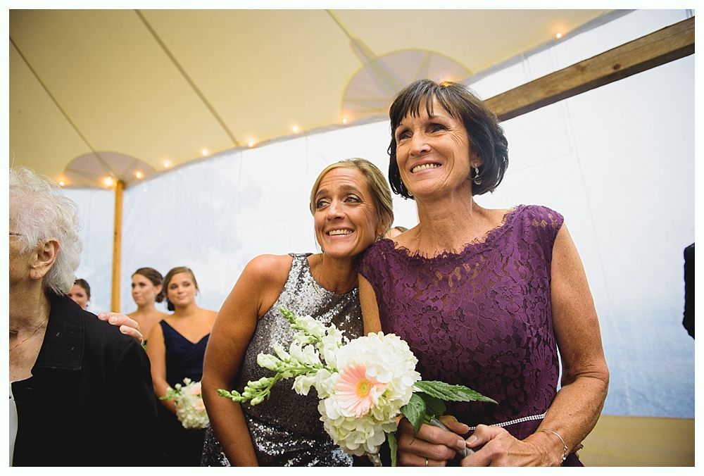 Woman in silver sequin dress and woman in purple dress smile, holding bouquet.