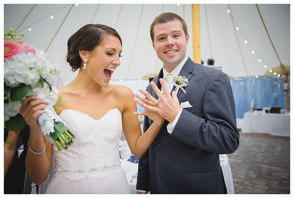 Bride and groom showing off rings, bride exclaiming with excitement, groom smiling, white dress and suit.