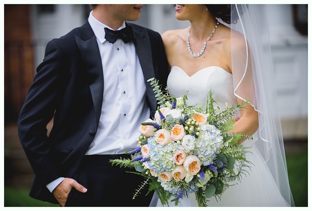 Bride and groom in formal attire embrace, holding a bouquet.