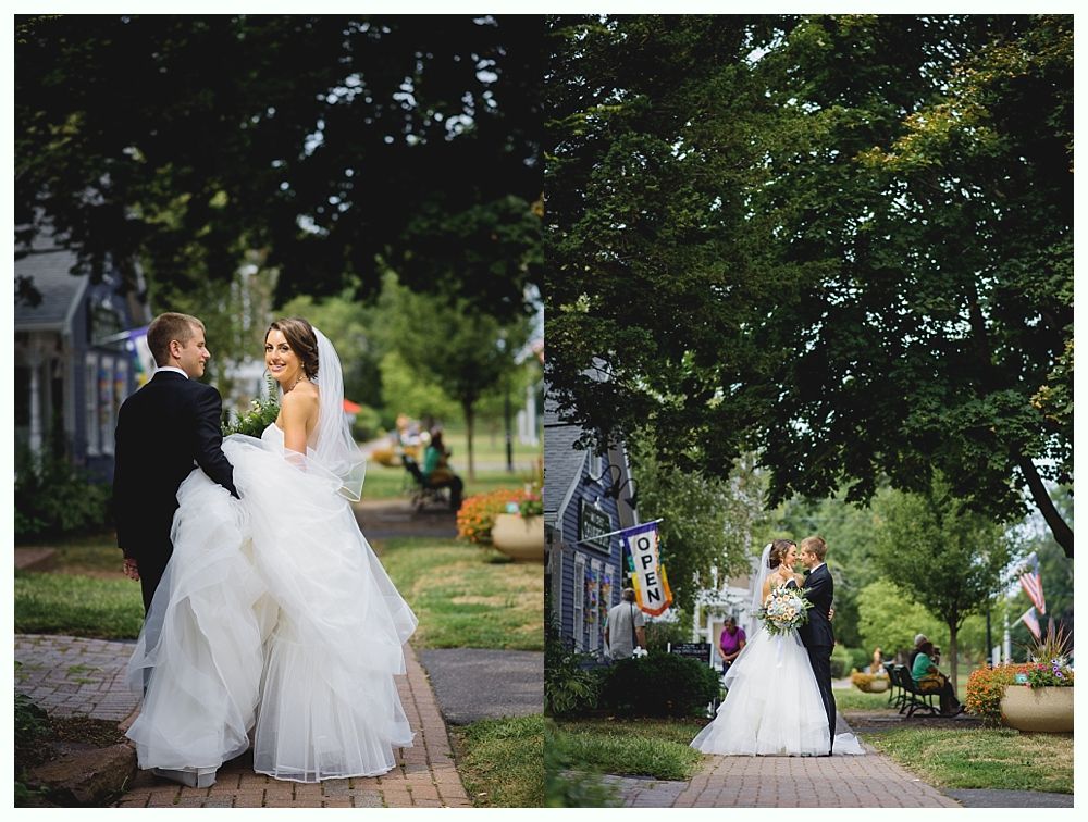 A bride and groom in formal attire walking on a brick path, smiling. Trees and buildings in background.