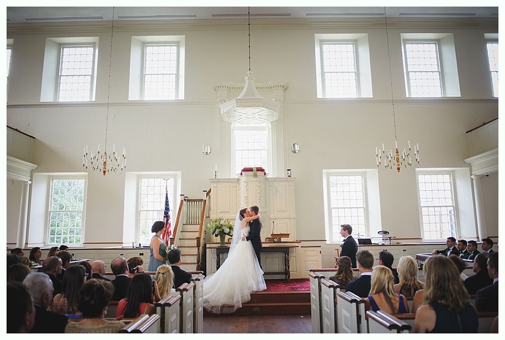 Wedding ceremony: couple kissing at altar in white church, guests seated.