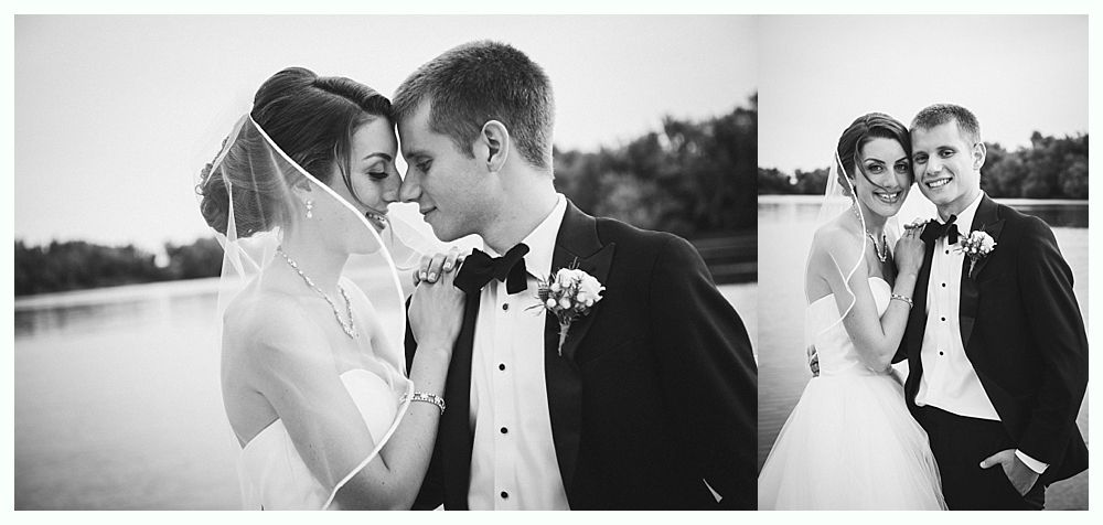 Wedding couple, embracing. Bride in veil, groom in tuxedo. Outdoors near water.