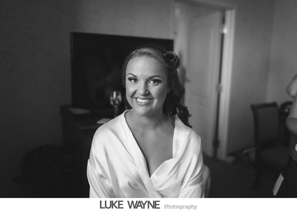 Woman in white robe smiles, hair styled, in a room with a TV and furniture.