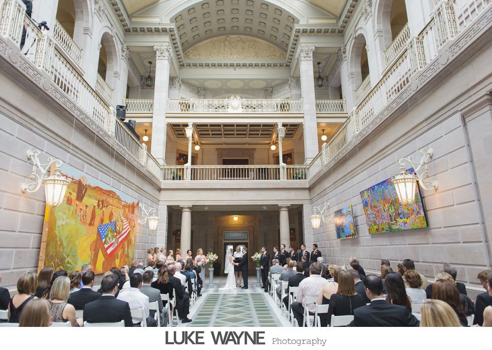 Wedding ceremony in ornate hall with couple at altar and guests seated.