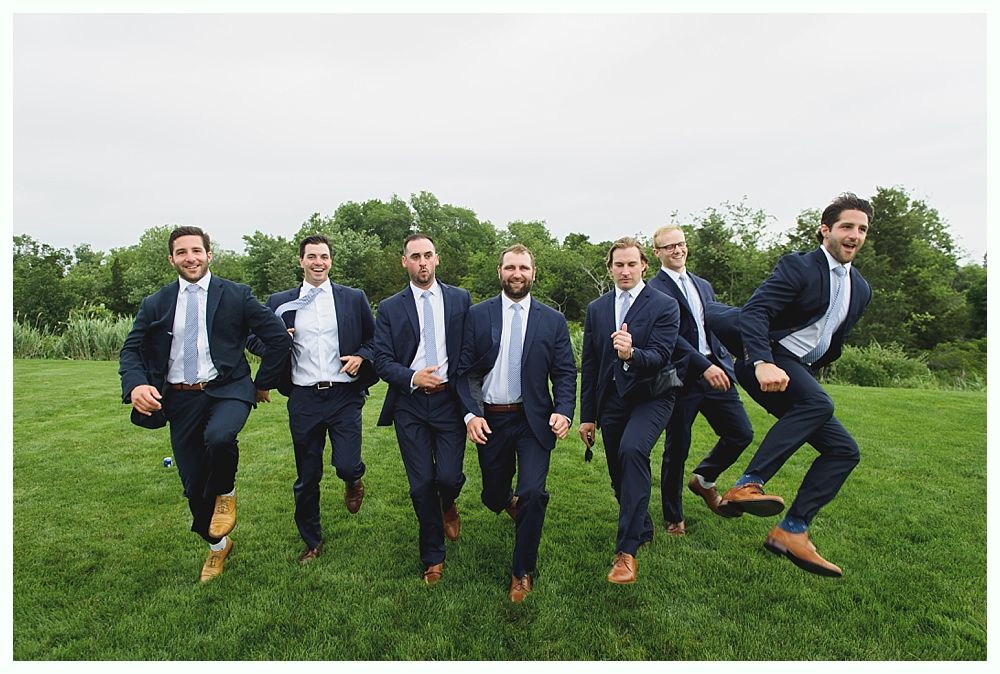 Seven men in blue suits run across a grassy field.