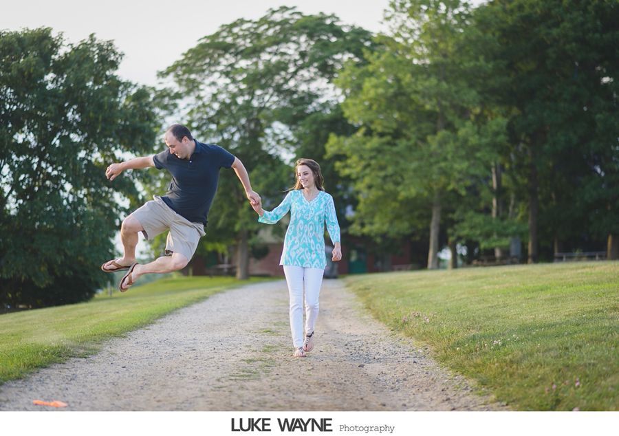 Man jumping, holding hands with woman walking on path; park setting.