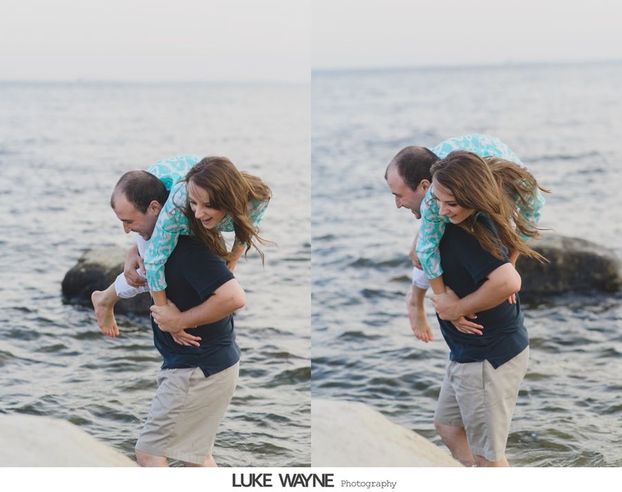 Man carrying a woman on his back in water, both smiling. They are near the sea on a sunny day.