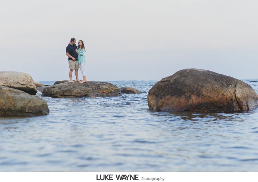 Couple standing on rocks in the ocean; dusk setting.