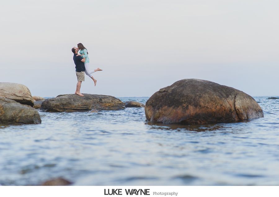 Man lifting woman on rocks in ocean.