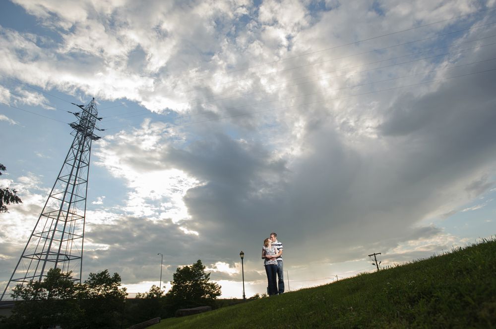 Person standing on a grassy hill next to a tall, metal structure against a cloudy sky.