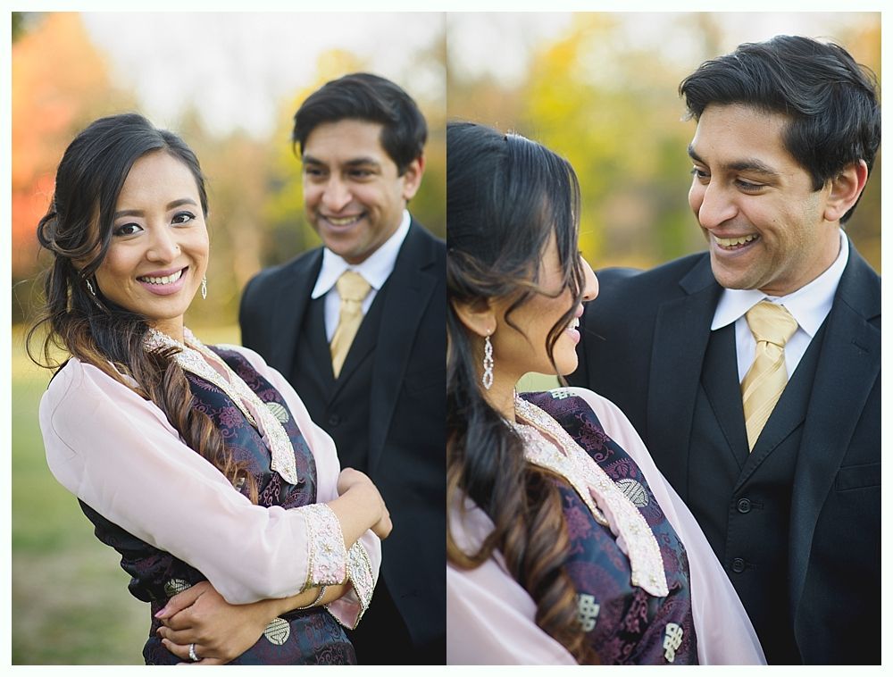 Couple smiling. Woman wears a pink blouse and patterned top. Man in black suit with yellow tie. Outdoors, trees in background.