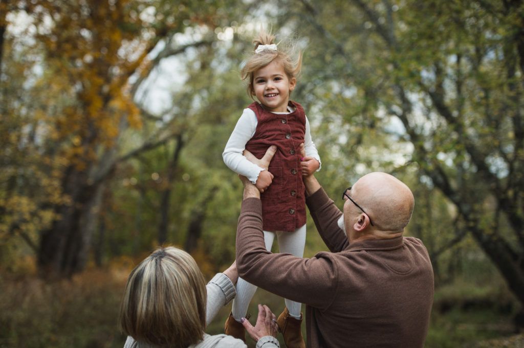 Person holding a child up in the air, outdoors. Child smiles. Forest setting.
