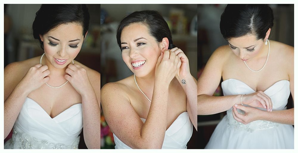 Bride in a white strapless gown putting on jewelry, smiling, indoor setting.