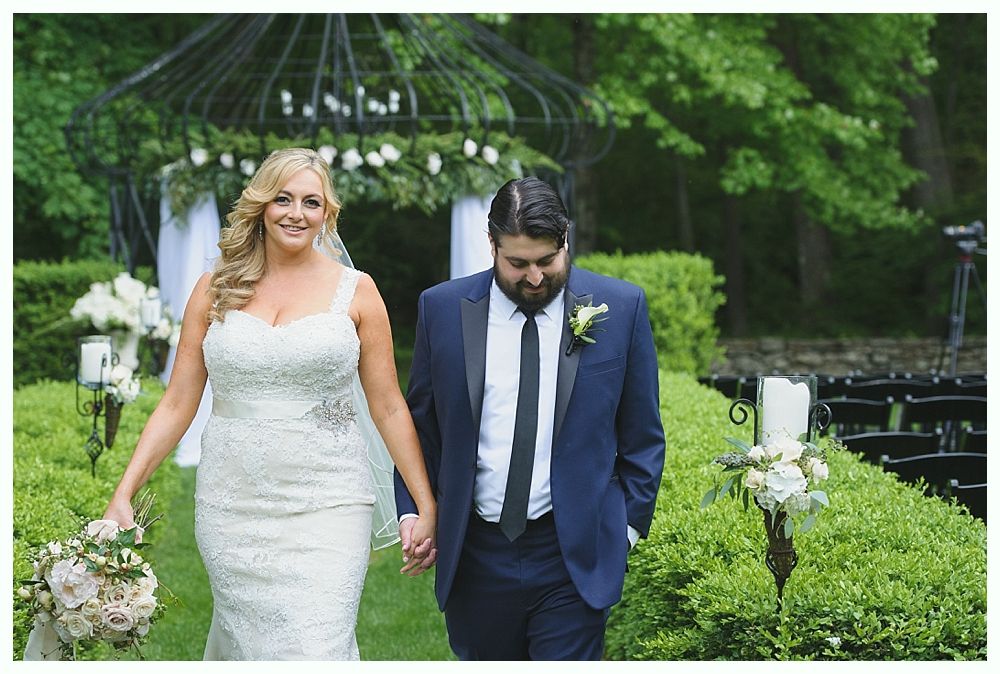 Bride and groom holding hands walking down a garden path after their wedding.