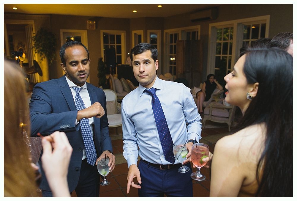 Two men and a woman conversing at an event, holding drinks. Interior lit by warm light.