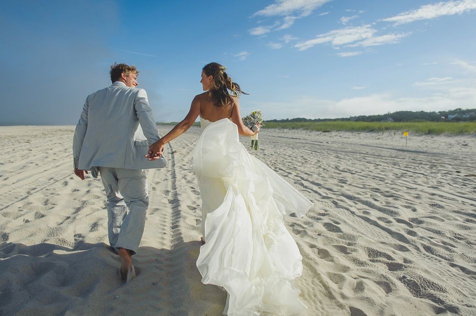 Bride and groom walk hand-in-hand on a sunny beach after their wedding.
