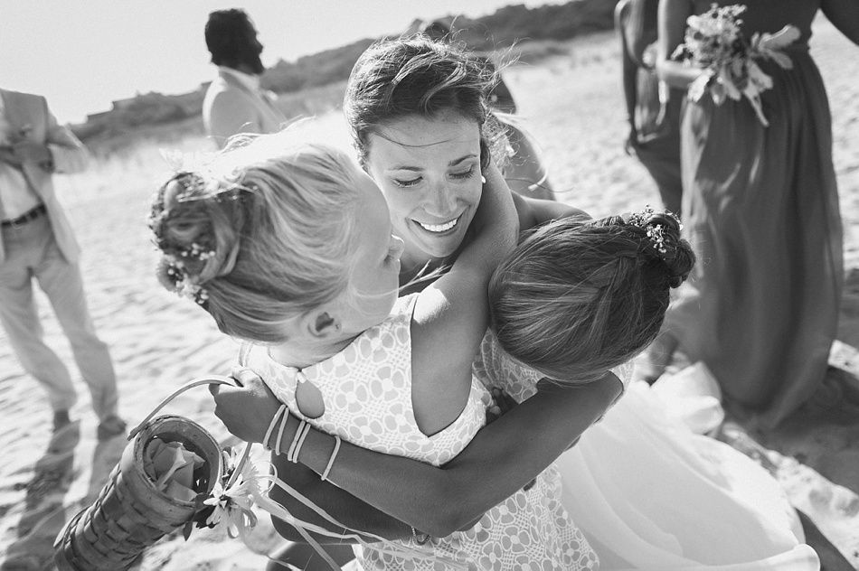Bride embraced by two children on a beach. All are smiling.