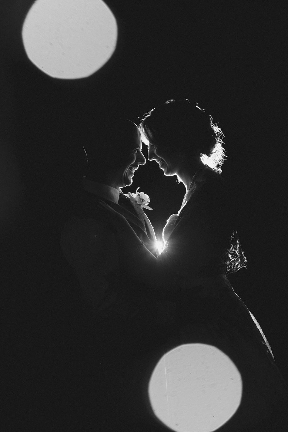 Silhouetted couple facing each other, illuminated by light, with bokeh circles in the dark.