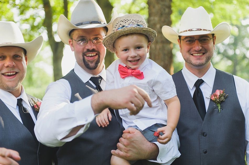 Four men and a child in cowboy hats and vests smile outdoors.