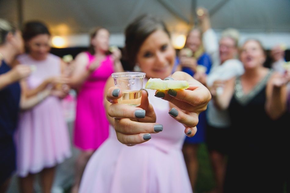 Woman holds shot of alcohol with lime, celebrating with friends outdoors.