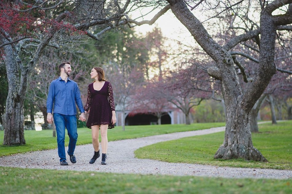 Couple holding hands, walking on a path in a park, trees and green grass surrounding.