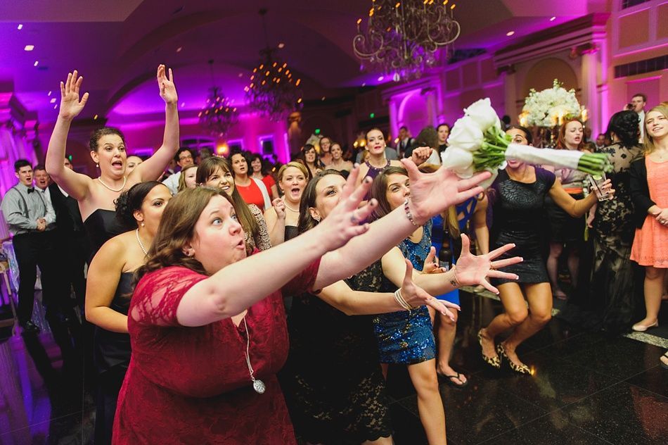 Guests reaching for a bouquet tossed in a wedding reception, purple lighting.