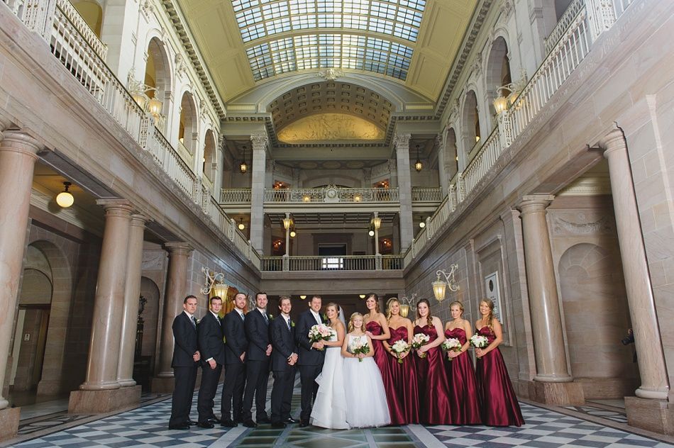 Wedding party in formal attire poses in ornate building hallway.
