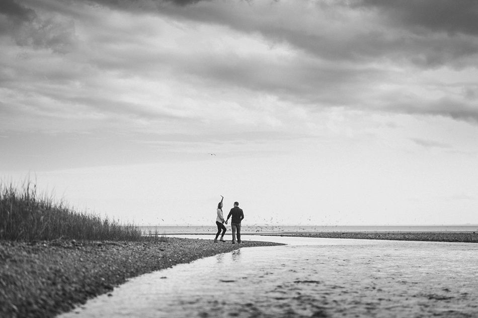 Couple standing in shallow water, one throwing something up. Cloudy sky over the beach.