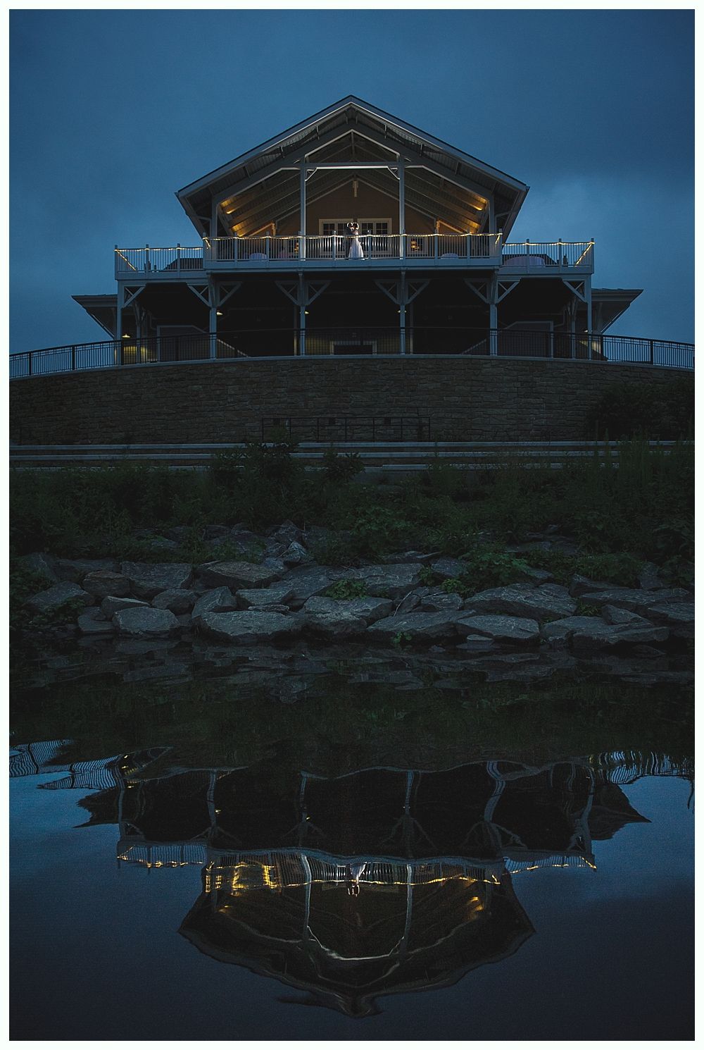 Wooden building with lights reflected in water at dusk.