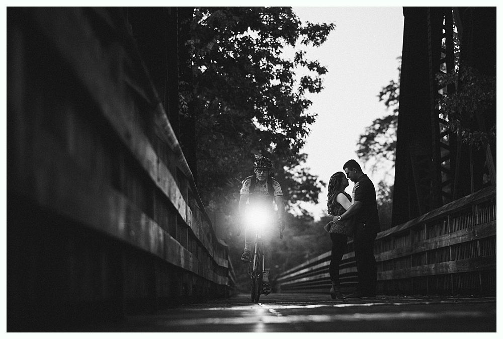 Couple embracing on a wooden bridge, bright light behind them. Black and white.