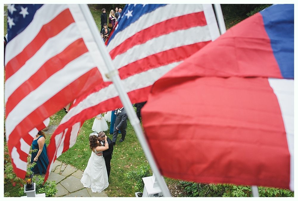 Wedding ceremony with bride and groom, two American flags, and a red flag.